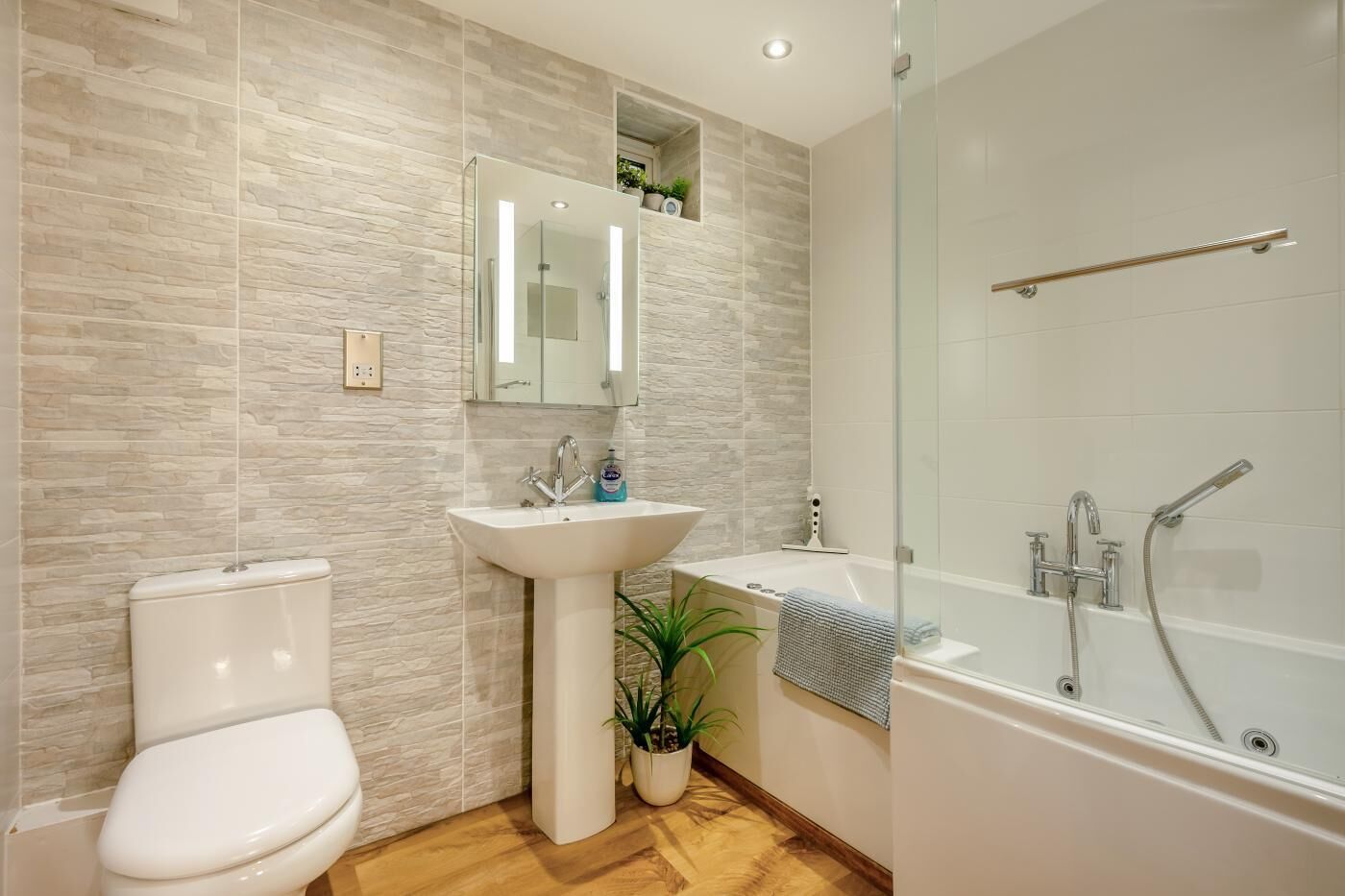 A modern bathroom with a toilet, pedestal sink, and glass-enclosed shower.