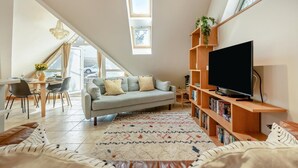 Uma sala de estar moderna com sofá, televisão, estante de livros e área de jantar com cadeiras e mesa.