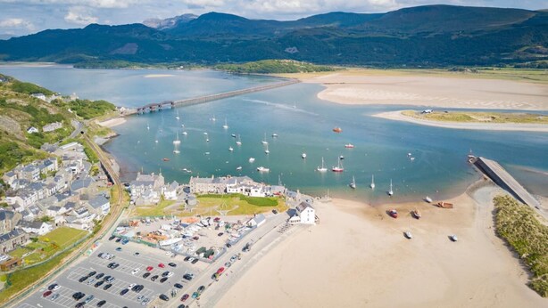 A coastal town with a marina, sandy beach, and mountainous backdrop. - 3 Bed in Brithdir (oc-c33971) (Brithdir)