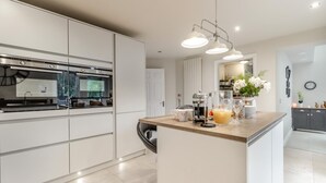 A modern kitchen with white cabinetry, a central island, and a built-in oven. - 3 Bed in Brithdir (oc-c33971) (Brithdir)