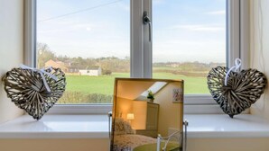Een kamer met uitzicht op een landelijk landschap, een nachtkastje met een lamp en een spiegel die de kamer weerspiegelt.