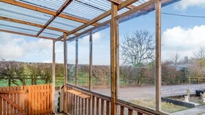 Een houten terras met een glazen omheining, een houten trap en uitzicht op een landelijk landschap.
