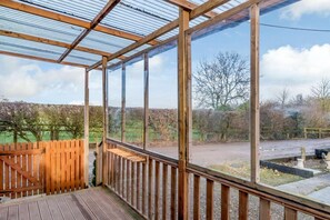 Eine Holzterrasse mit Glasumrandung, eine Holztreppe und Blick auf eine ländliche Landschaft.
