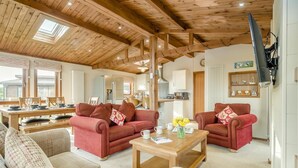 A cozy living room with a wooden ceiling, two red sofas, a wooden coffee table, and a dining area with a wooden table and chairs. - 3 Bed in Whitby (oc-wa057) (Runswick Bay)