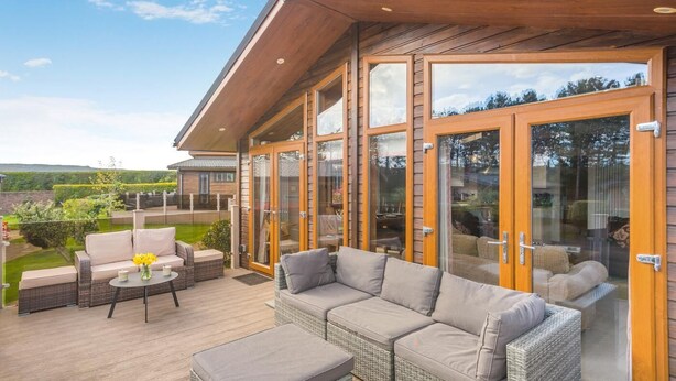 A covered outdoor seating area with wicker furniture and glass doors. - 3 Bed in Whitby (oc-wa057) (Runswick Bay)