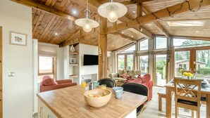 A spacious living area with a wooden ceiling, a dining table with chairs, a kitchen counter with a fruit bowl, and a television mounted on the wall. - 3 Bed in Whitby (oc-wa057) (Runswick Bay)