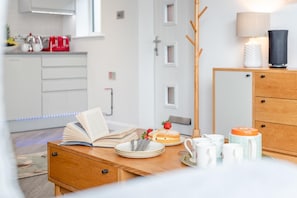 A modern kitchen with white cabinets, a wooden dining table, and a coffee station. - 2 Bed in Padstow (oc-p00655) (Padstow)