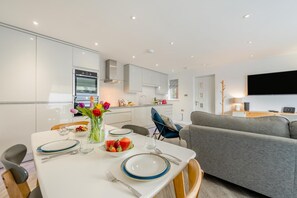 Eine moderne Küche mit weißen Schränken, einem Esstisch für vier Personen und einem grauen Sofa im Wohnbereich.