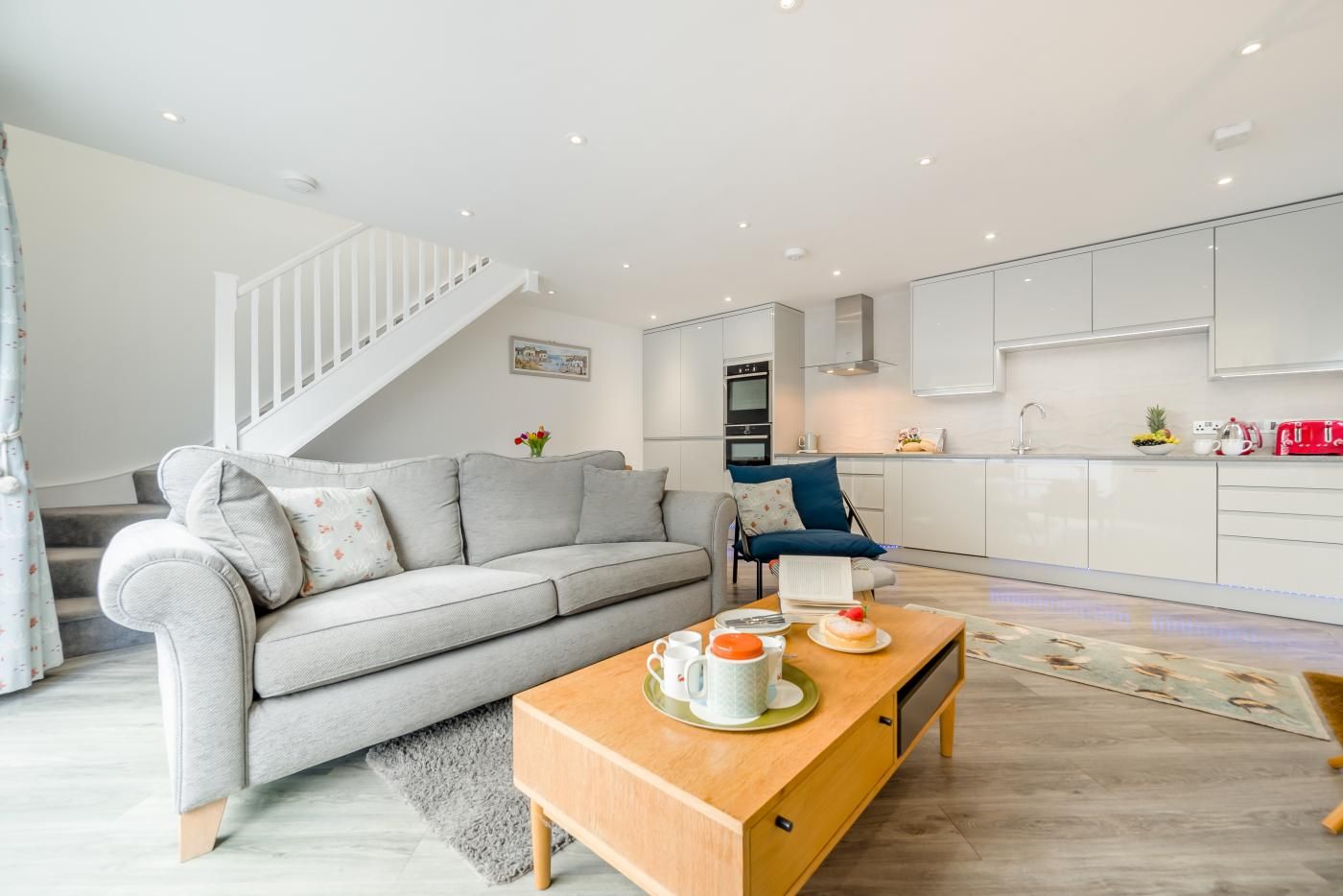 A modern living room with a grey sofa, a wooden coffee table, and a staircase leading to an upper floor.