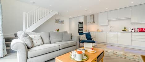 A modern living room with a grey sofa, a wooden coffee table, and a staircase leading to an upper floor.