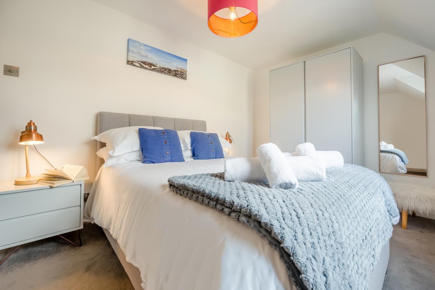 Ein modernes Schlafzimmer mit einem großen Bett, einem Nachttisch mit Lampe, einem Spiegel und einem Gemälde an der Wand.