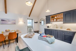 Eine moderne Küche mit dunklen Schränken, einer weißen Arbeitsplatte und einem Essbereich mit orangefarbenen Stühlen.