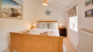 A bedroom with a wooden bed, a star decoration, and a beach painting on the wall. - 3 Bed in Sedgeford (oc-1827) (Sedgeford)