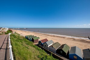 A beach with a row of beach huts along the shore, a pier in the distance, and a clear blue sky. - 3 Bed in Southwold (oc-marl) (Southwold)