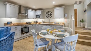 Une cuisine moderne avec des meubles blancs, un îlot central et un coin repas comprenant des chaises et une table blanches, le tout préparé pour le petit-déjeuner.