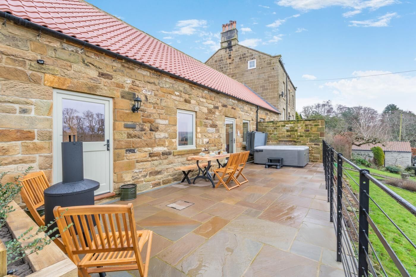 A stone building with a tiled roof, a patio with a table and chairs, and a hot tub.