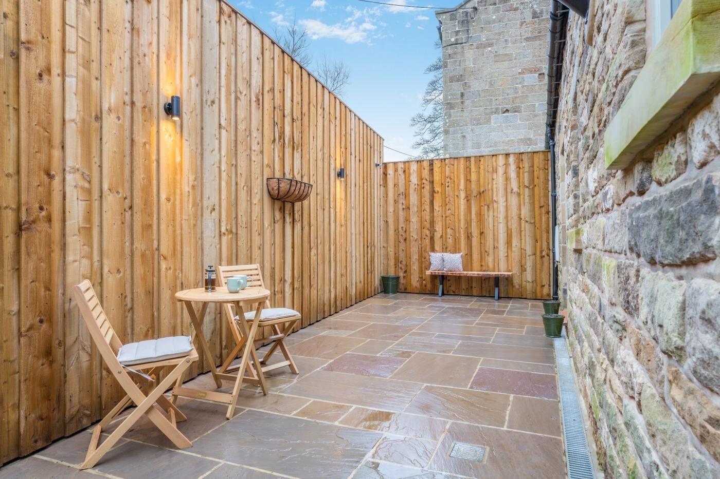 Une terrasse en bois avec un sol en pierre, un banc en bois et une table avec des chaises.
