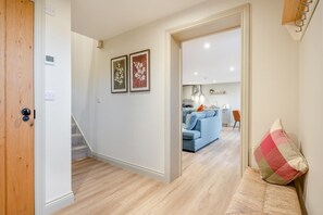 A hallway leading to a living area with a blue sofa, a kitchen in the background, and a wooden door on the left. - 2 Bed in Castleton (oc-f34013) (Castleton)
