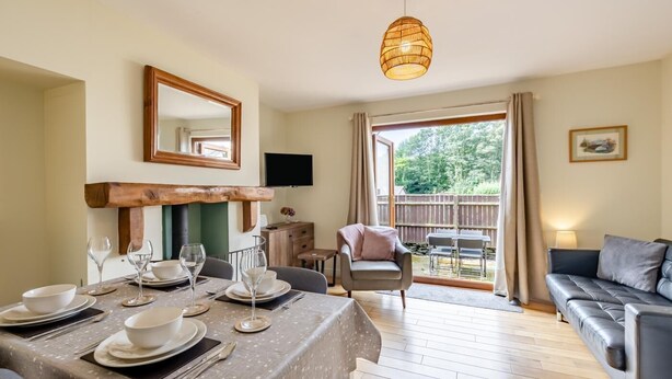 A dining area with a table set for four, a sofa, a TV mounted on the wall, and a view of the outdoors. - 2 Bed in Nr. Newby Bridge (oc-ld168) (Backbarrow)