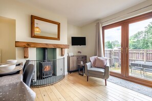 A cozy living room with a fireplace, a television, a dining area with a table and chairs, and a balcony with a view. - 2 Bed in Nr. Newby Bridge (oc-ld168) (Backbarrow)