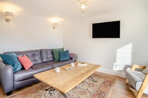 Een moderne woonkamer met een leren bank, een houten salontafel en een flatscreen televisie aan de muur.