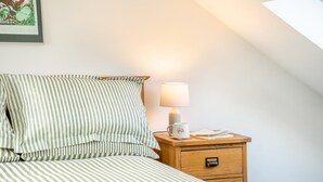 Un letto rifatto con biancheria a righe, una lampada da comodino, una tazza e un piccolo comodino in legno con un cassetto.