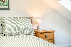 Ein ordentlich bezogenes Bett mit Streifenmuster, eine Nachttischlampe, eine Tasse und ein kleiner Nachttisch aus Holz mit einer Schublade.