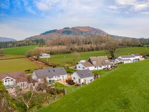 Un village rural avec des maisons, une colline en arrière-plan et un champ verdoyant.