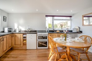 Una cocina moderna con armarios de madera, horno empotrado, microondas y un comedor con mesa y sillas de madera.
