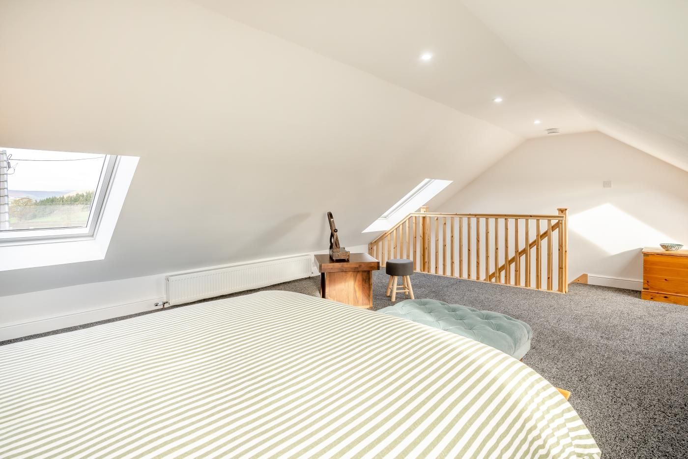 A spacious attic bedroom with a large bed, a desk, and a staircase leading to an upper level.