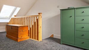 Una stanza con un settimino in legno, un armadietto verde, una scala in legno e un lucernario.