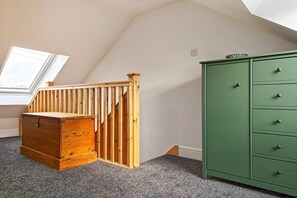 Ein Zimmer mit einer Holzkommode, einem grünen Schrank, einer Holztreppe und einem Oberlicht.