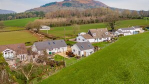 Un pueblo rural con casas, una colina al fondo y un campo verde.