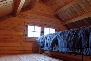 Une pièce de cabane en bois comprenant un lit, une fenêtre et un plafond en pente.