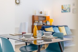 A dining table with a glass top, surrounded by blue chairs, a bottle of orange juice, and two bowls. - 1 Bed in Cromer (oc-1844) (Cromer)