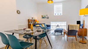 Ein modernes Wohnzimmer mit einem Glastisch, Smaragdgrün-Stühlen, einem blauen Sofa und einer gelben Lampe.