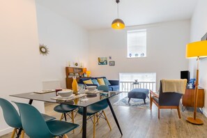 A modern living room with a glass dining table, teal chairs, a blue sofa, and a yellow lamp. - 1 Bed in Cromer (oc-1844) (Cromer)