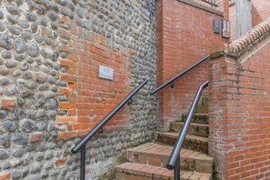 A staircase with metal handrails, a stone wall, and a brick wall with a small sign. - 1 Bed in Cromer (oc-1844) (Cromer)