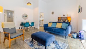 Ein modernes Wohnzimmer mit einem blauen Sofa, einem Holzstuhl, einem Esstisch mit Stühlen und Pendelleuchten.