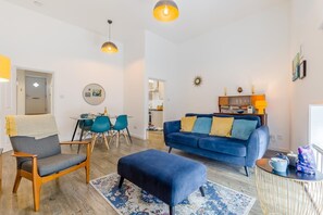 A modern living room with a blue sofa, a wooden chair, a dining table with chairs, and pendant lighting. - 1 Bed in Cromer (oc-1844) (Cromer)