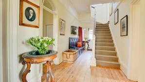 A hallway with a staircase, framed pictures, a potted plant, and a wicker basket. - 6 Bed in Lower Bodham (oc-1830) (Bodham)