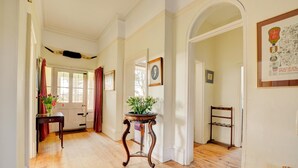 A hallway with wooden flooring, a door with red curtains, a small table with a plant, and a framed picture on the wall. - 6 Bed in Lower Bodham (oc-1830) (Bodham)