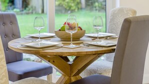 Een ronde houten eettafel met een schaal fruit en wijnglazen, omringd door gestoffeerde stoelen.