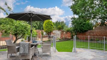An outdoor patio with a table and chairs, a large umbrella, and a brick wall in the background.