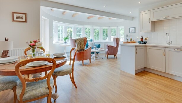 Un comedor amplio con mesa y sillas de madera, una cocina con armarios blancos y ventanas grandes que dejan entrar luz natural.