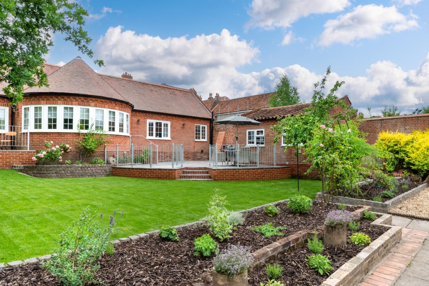 A brick house with a curved roof, a fenced patio, and a well-maintained garden.