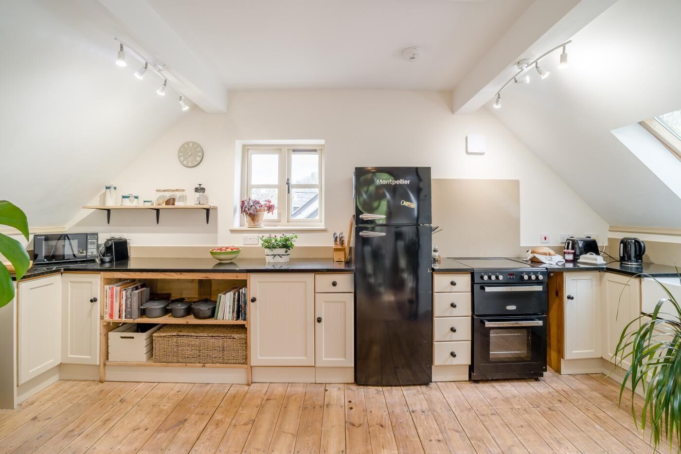 Een moderne keuken met een zwarte koelkast, een kookplaat en een magnetron. Er zijn houten keukenkastjes en een raam boven de spoelbak.
