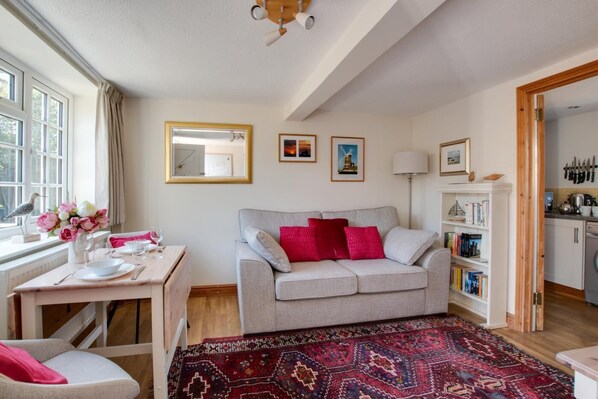A cozy living room with a grey sofa, red cushions, a wooden coffee table, a patterned rug, and a bookshelf.