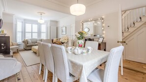 A dining area with a table set for four, surrounded by wicker chairs, a chandelier, and a staircase leading to an upper floor. - 4 Bed in Southwold (oc-23str) (Southwold)