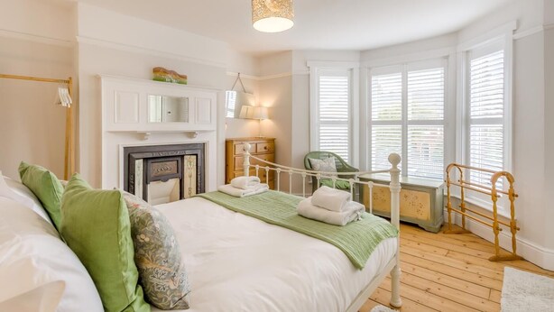 A bedroom with a bed, a fireplace, a window with shutters, and a hanging chair. - 4 Bed in Southwold (oc-23str) (Southwold)